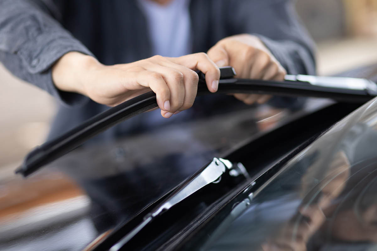Hände tauschen einen Scheibenwischer an der Windschutzscheibe eines Autos aus.